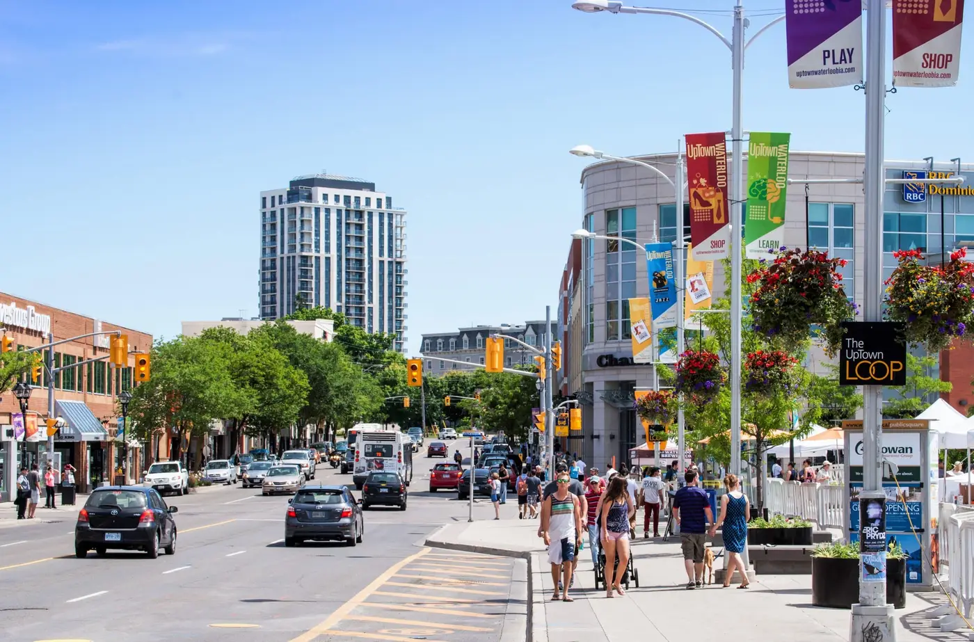 A busy summer day on King Street in Uptown Waterloo — people walking past shops and patios under UpTown Waterloo banners and hanging flower baskets, a short walk from Chameleon's boardrooms